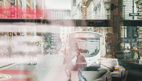 En stadsmiljö, två personer rör sig framför en buss