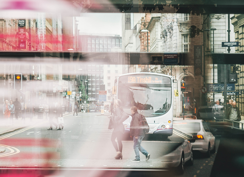 En stadsmiljö, två personer rör sig framför en buss
