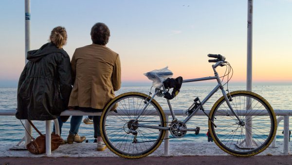 Två personer sitter och tittar på en solnedgång vid vattnet, en cykel står parkerad bredvid