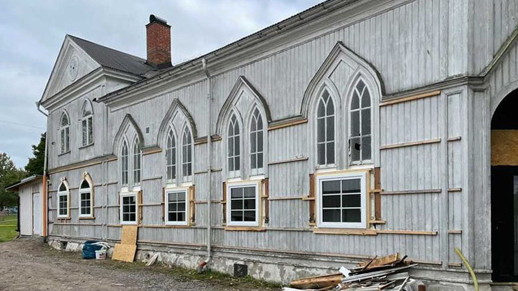 En byggnad som ser ut som en kyrka, fönstren renoveras - nya fönster ser annorlunda ut än de befintliga