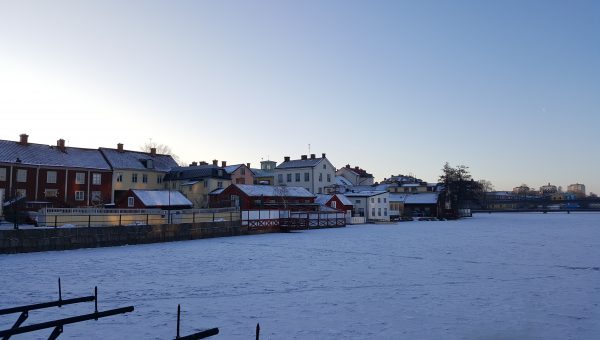 Ett snötäckt fält med bebyggelse i bakgrunden
