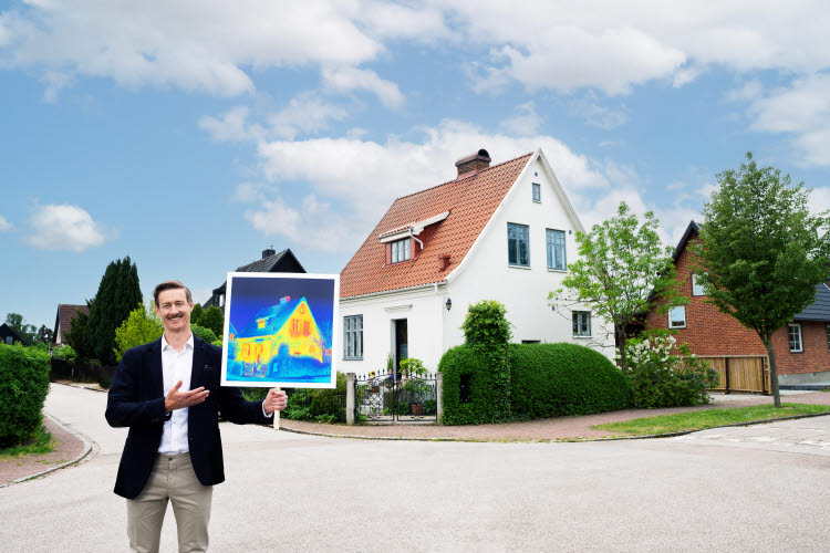 Boverket lanserar energiguide för småhusägare.Foto: Infab En man håller i en skylt, står framför en vit villa.