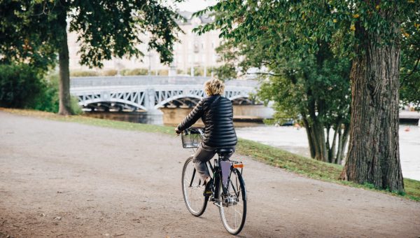 Stöd från Klimatklivet på väg mot en fossilfri stad. Kvinna cyklar på promenadväg längs vattnet. Foto: johner.se/Maskot Bildbyrå AB