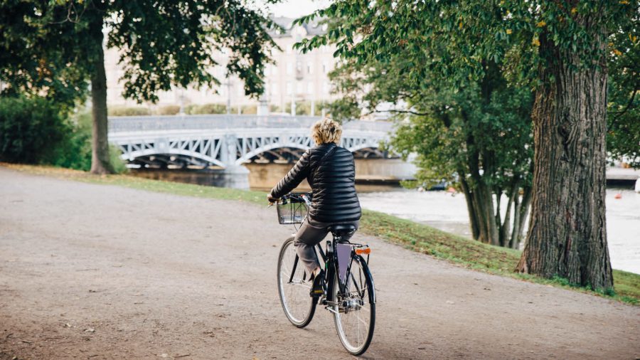 Stöd från Klimatklivet på väg mot en fossilfri stad. Kvinna cyklar på promenadväg längs vattnet. Foto: johner.se/Maskot Bildbyrå AB