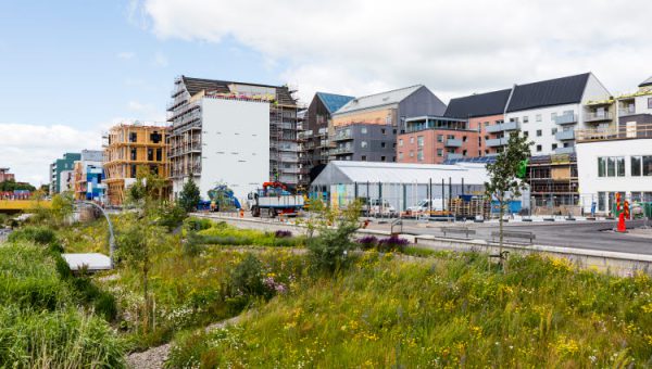 Stöd för hållbar stadsutveckling. Foto på byggnader under uppförande, grässlänt och äldre byggnader.