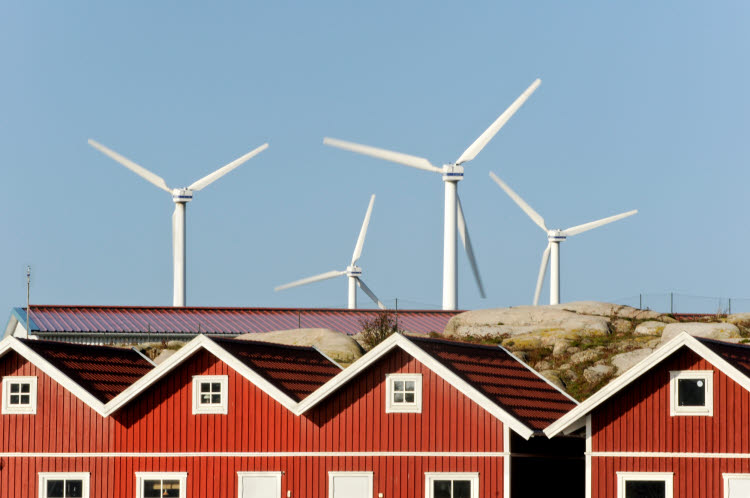 Klimatneutrala och socialt hållbara kommuner 2024. Foto på små röda hus med vindkraftverk i bakgrunden.