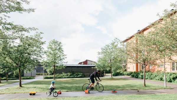 Utlysning: Klimatneutrala och socialt hållbara kommuner 2024. Foto på vuxen och barn som cyklar i ett bostadsområde.