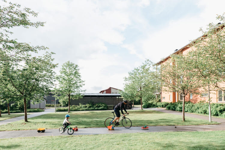Utlysning: Klimatneutrala och socialt hållbara kommuner 2024. Foto på vuxen och barn som cyklar i ett bostadsområde.