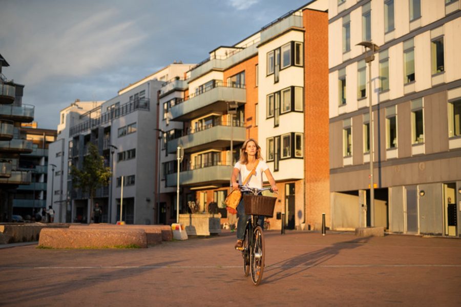 En kvinna cyklar med hus i bakgrunden.